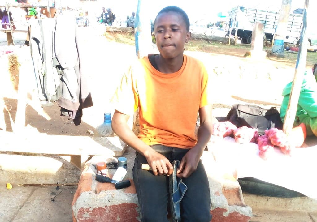 Bright boy sewing shoes while seeking financial assistance to join Form 1
