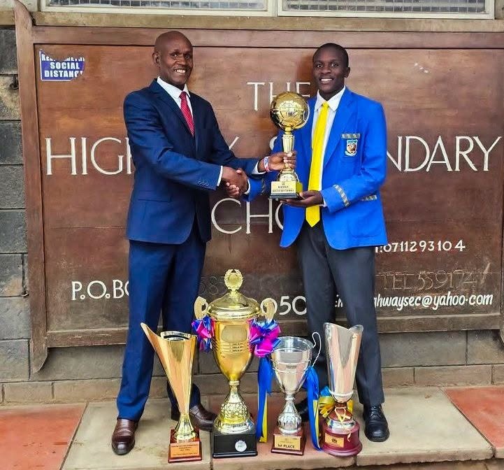 Chief Principal Irungu Nduati receives a trophy from a Highway Senior School student, part of the haul of accolades the institution collected under his six-year tenure